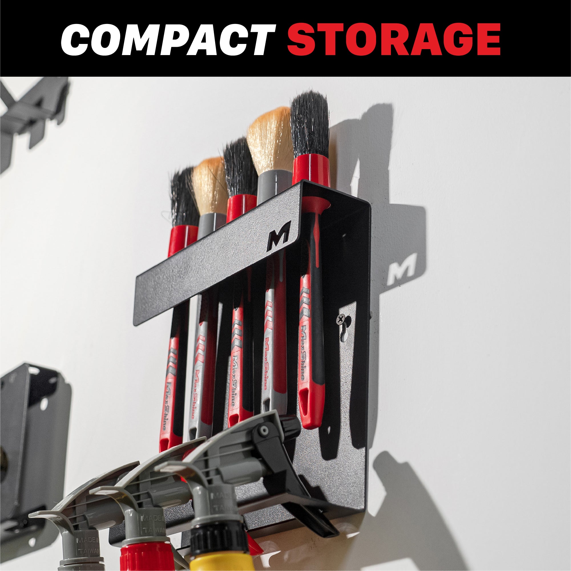 A black wall-mounted brush holder labeled with a large letter M cutout, holding several red-handled brushes. The image includes a top banner reading 'COMPACT STORAGE' H06C Wall Mount Tool Holder