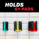 Three black wall-mounted polishing pad holders on a white tiled wall, showing green, yellow, and red foam pads inside. A black banner at the top reads 'HOLDS 6+ PADS' in white and red text. Polisher Pads Holders